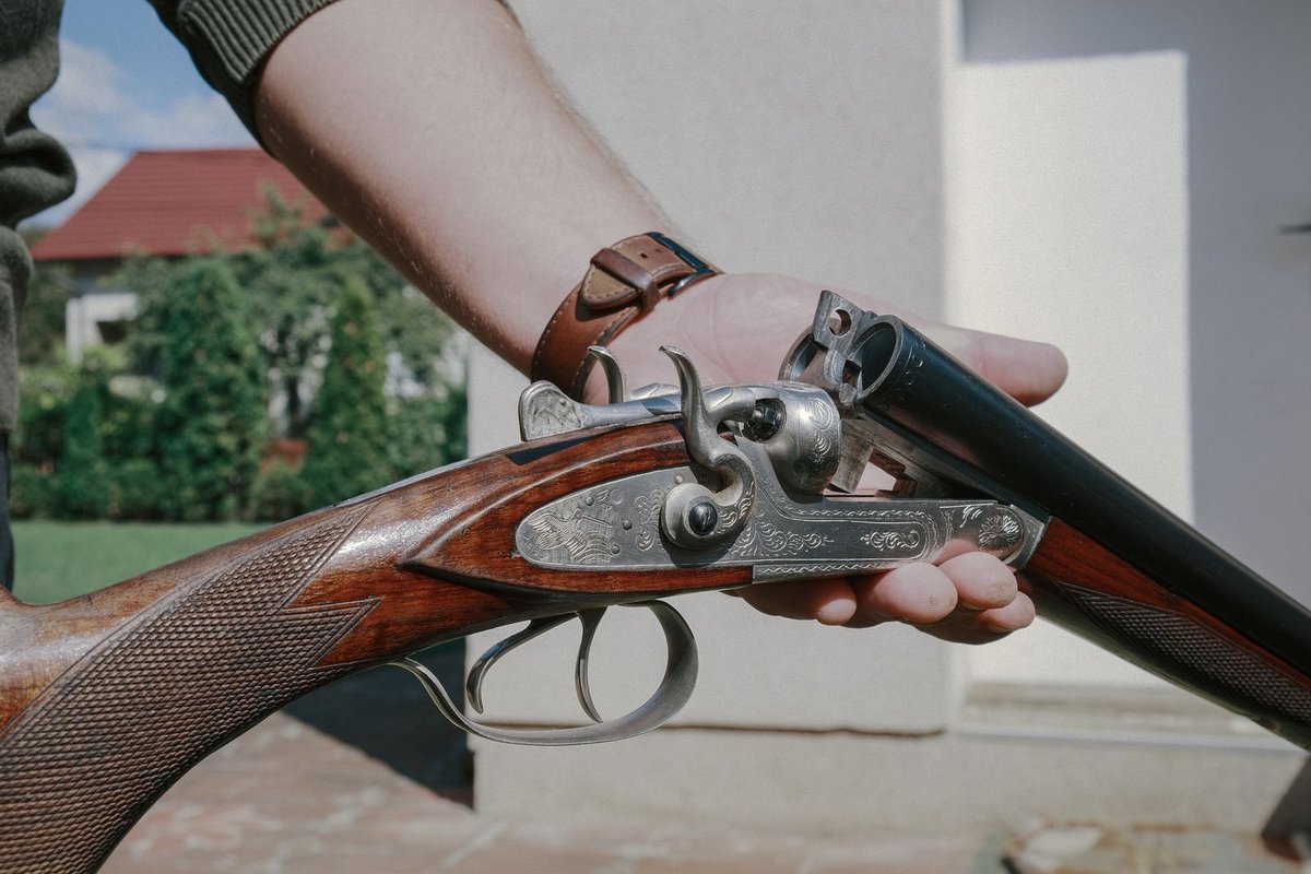 Open side-by-side double-barrel shotgun with engraved receiver and walnut stock held outdoors.