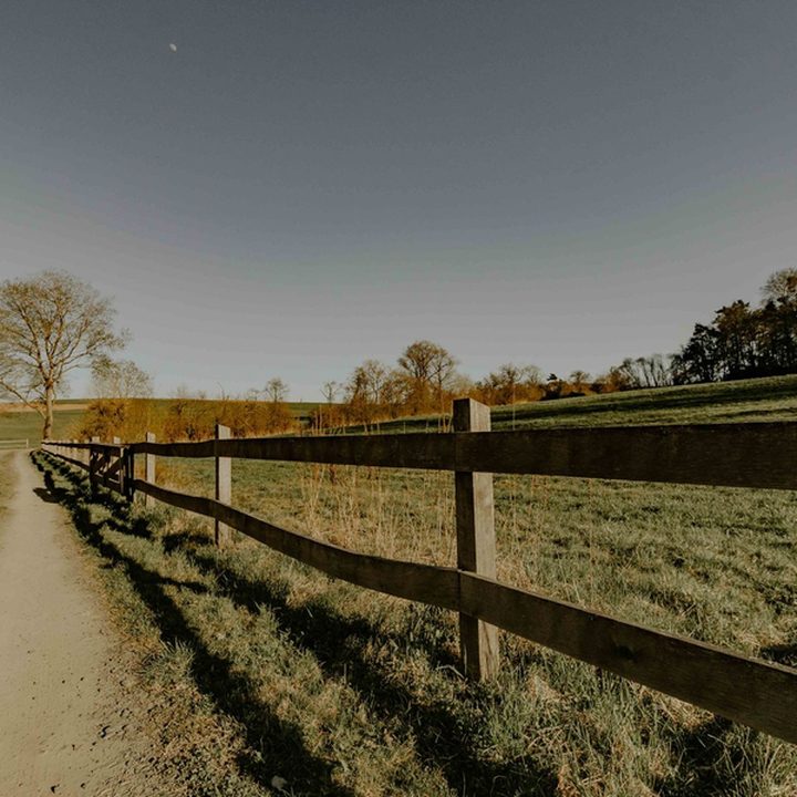 Rural dirt path along a wooden fence line at golden hour, the mark for walk-in access.